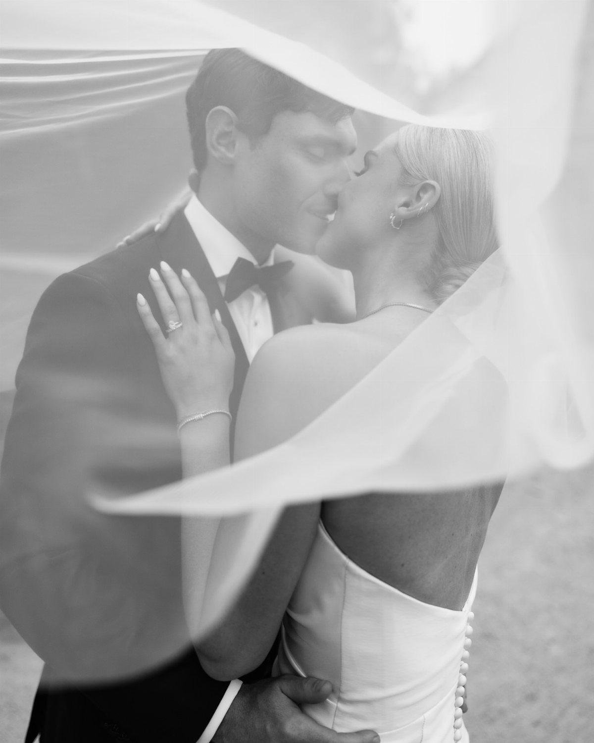 Bride and groom kissing while draped under a sheer white bridal veil.