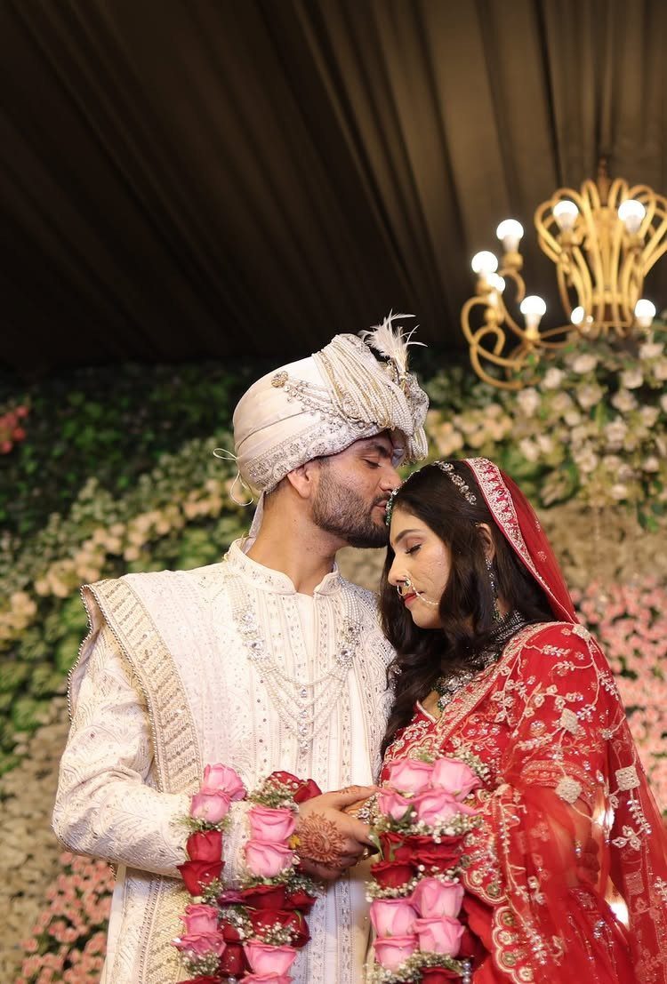 Groom in white sherwani kissing the forehead of a bride in red lehenga.