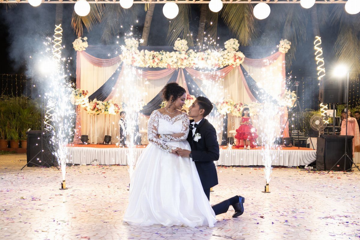 Bride and groom posing on a dance floor with sparkling pyrotechnics and floral backdrop.