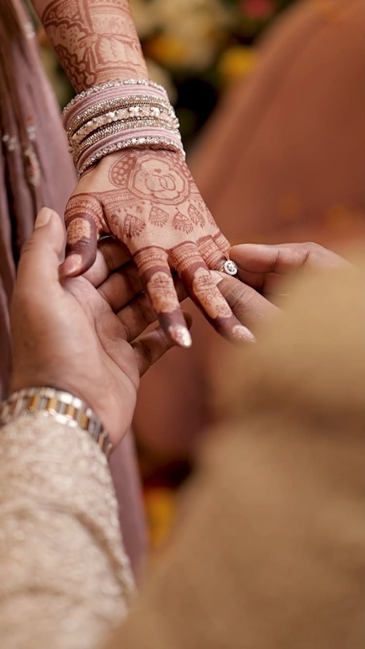 Hands of a couple during a wedding ring exchange with detailed henna art.
