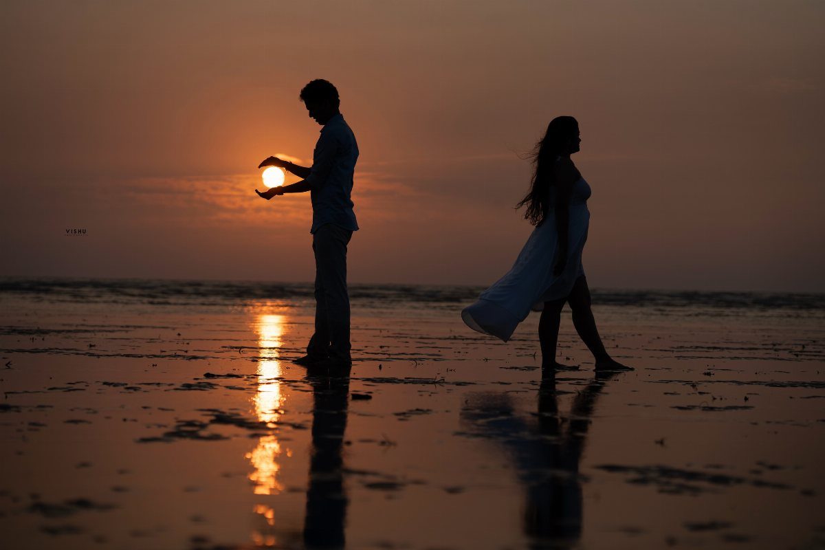 Silhouetted couple on a beach at sunset with the man cradling the sun.