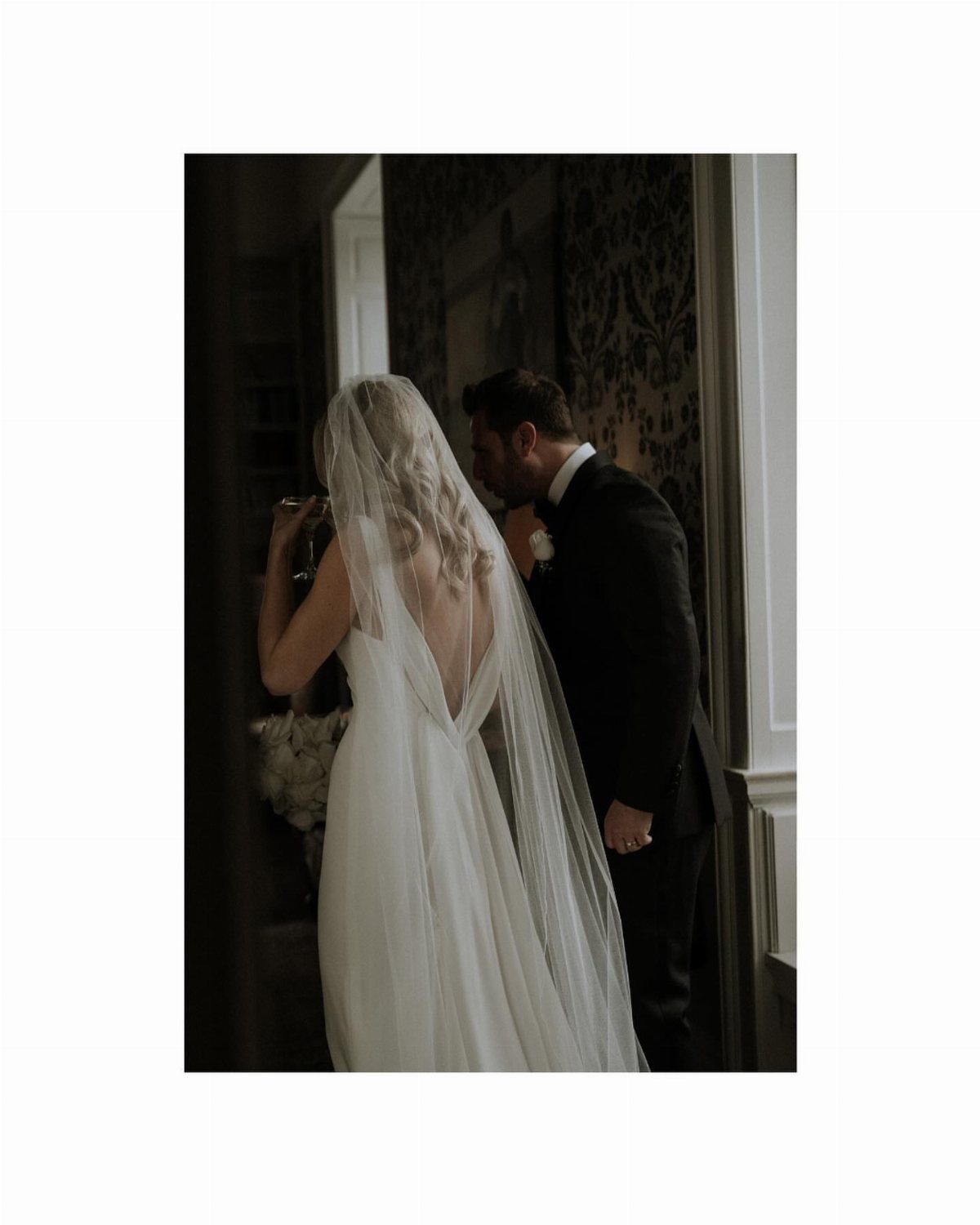 Bride and groom standing together from behind in a dimly lit room.