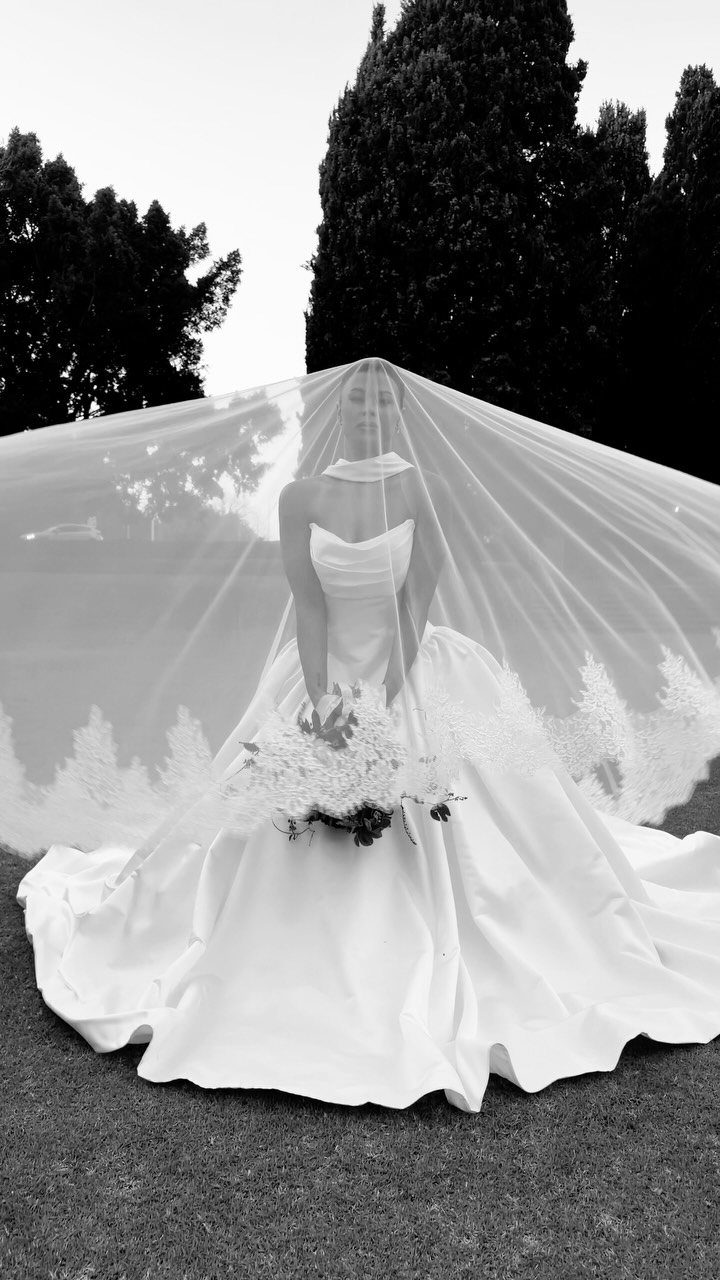 Bride in a white wedding gown posing under a wide, billowing bridal veil.