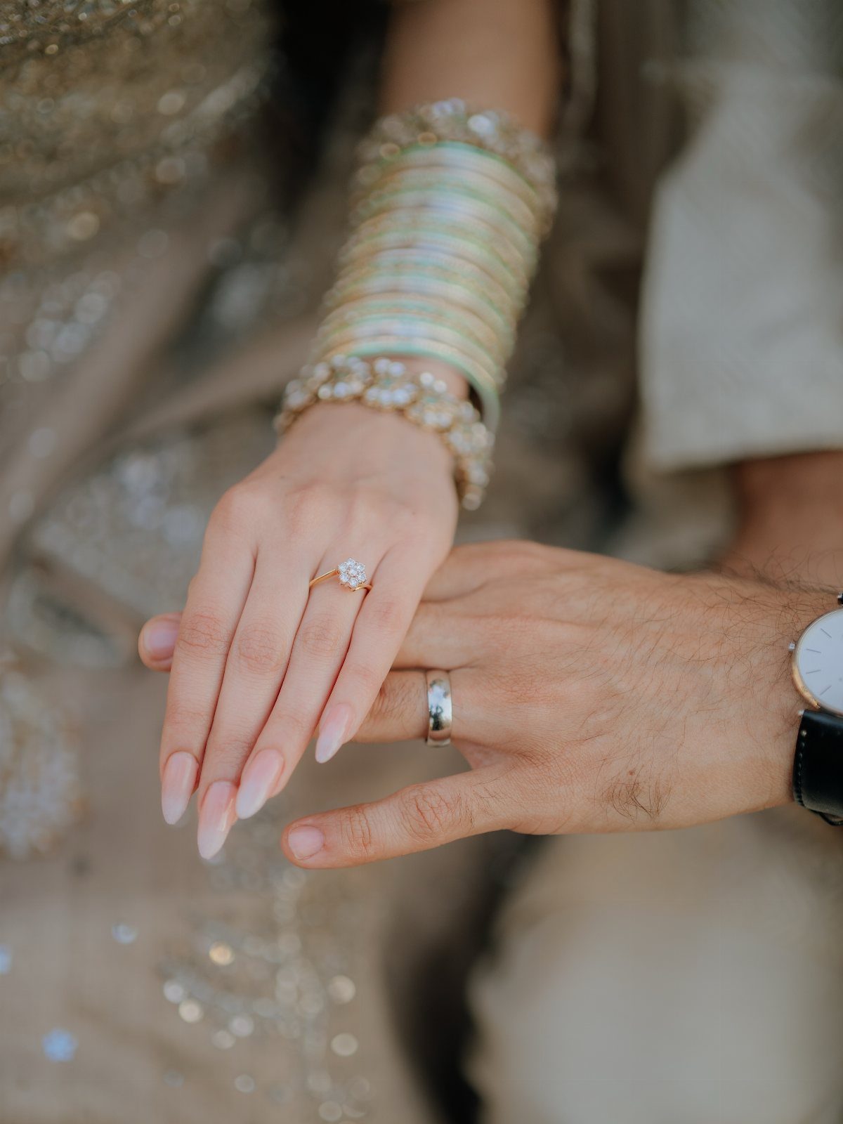 Couple's hands showing a diamond engagement ring and a silver wedding band.