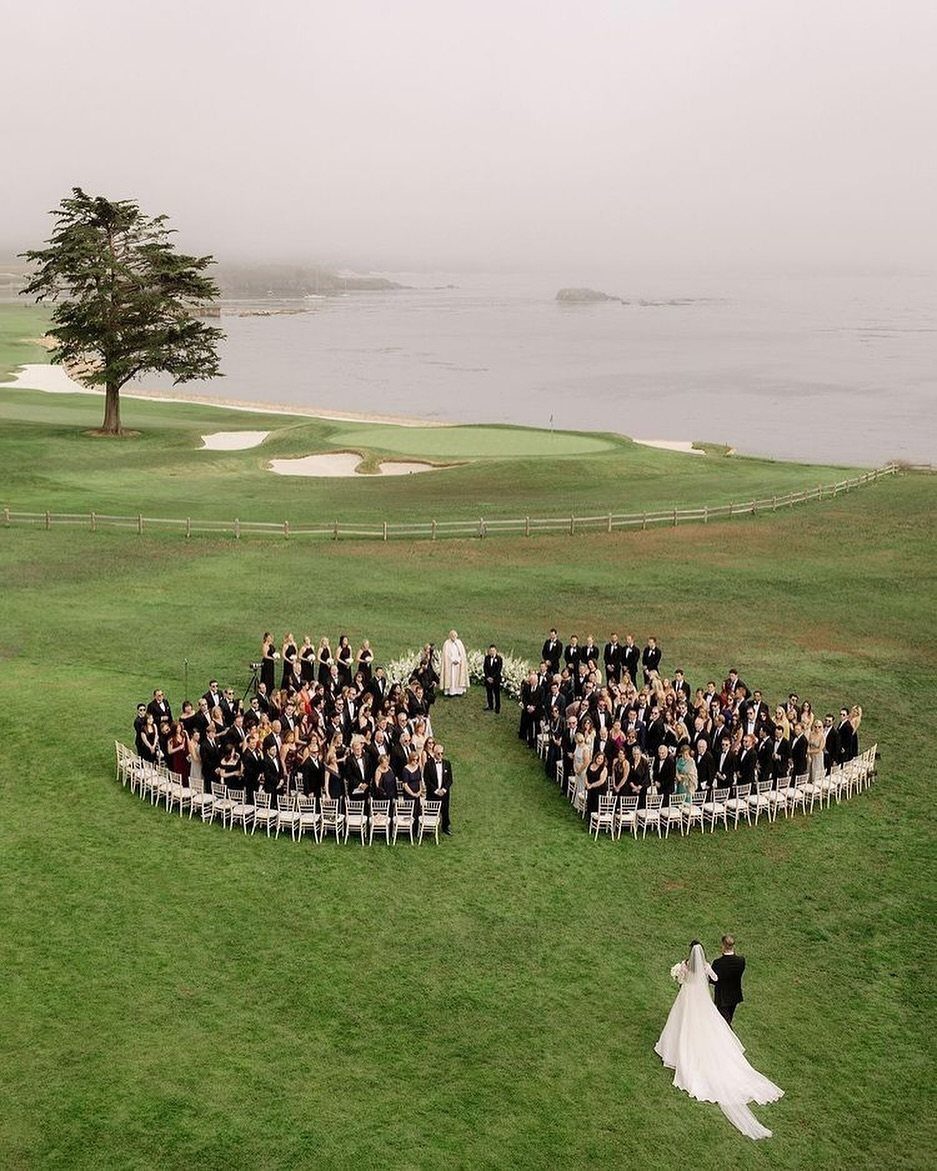 Aerial view of wedding guests seated in a heart shape on green grass.