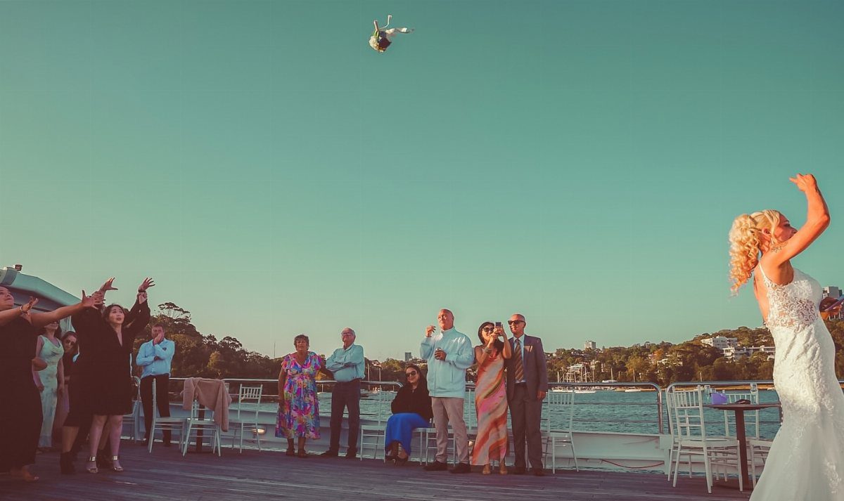 Bride in white gown tossing her bouquet to guests on a boat deck
