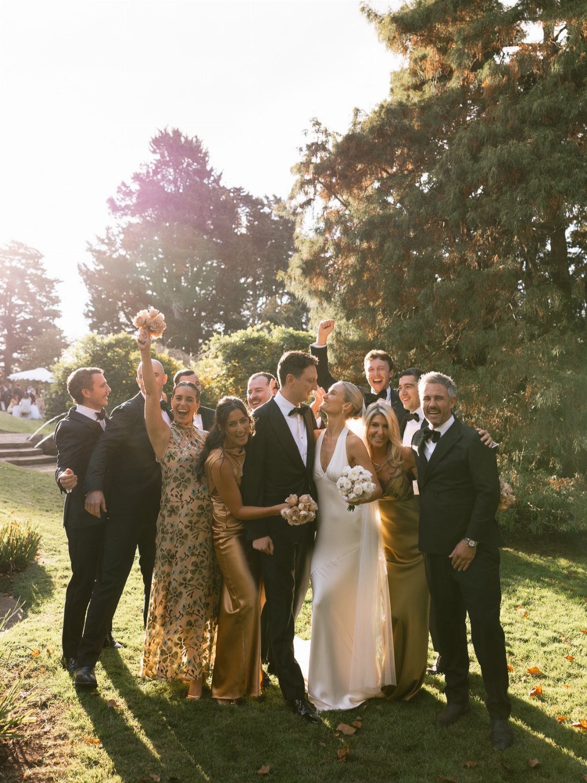 Wedding party posing and cheering outdoors with the bride and groom in center.