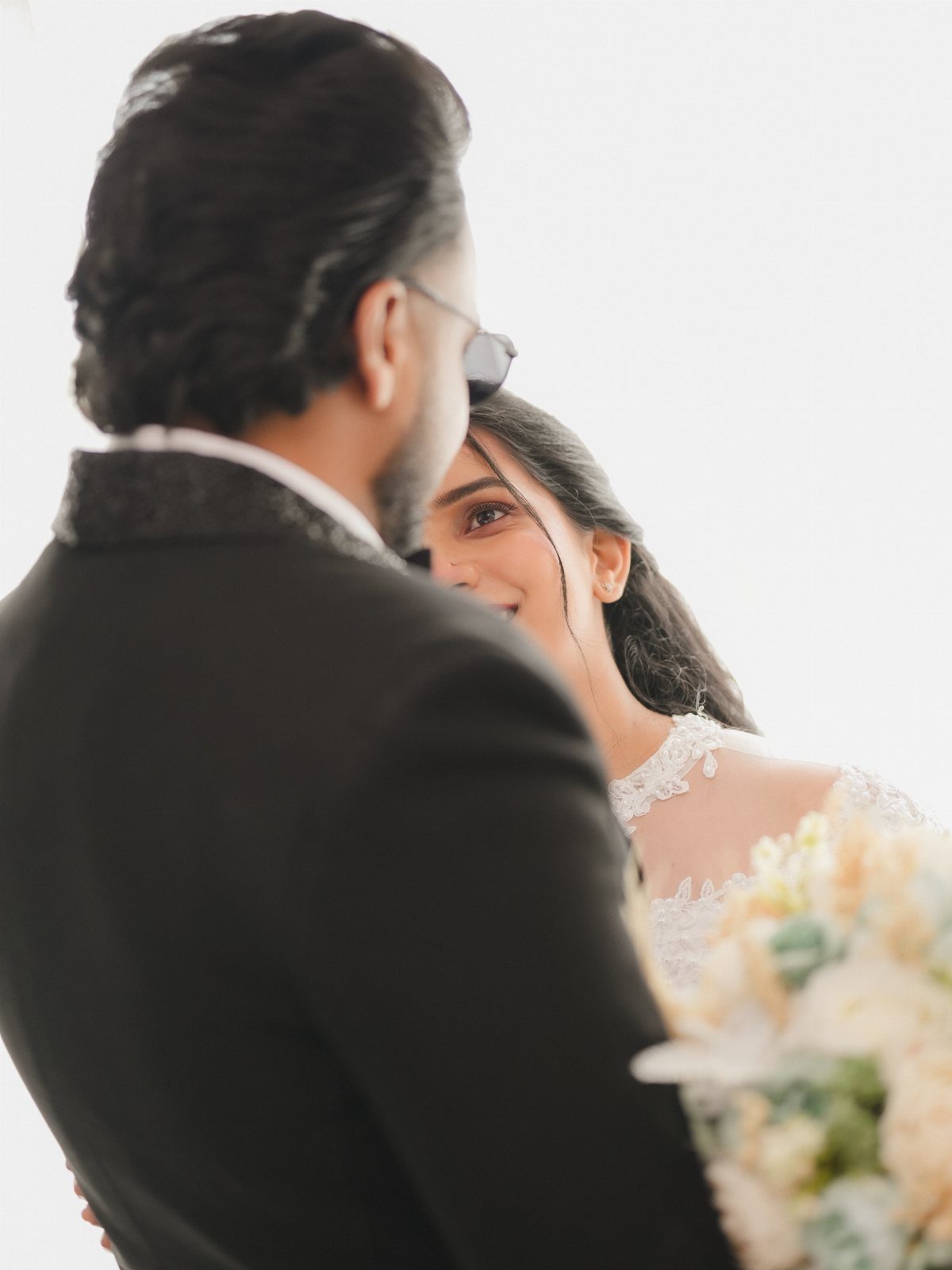 Smiling bride in white lace dress looking up at groom in black suit
