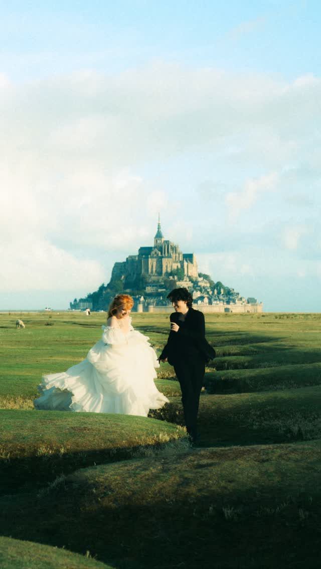 Bride and groom running through a grassy field with Mont Saint-Michel in background