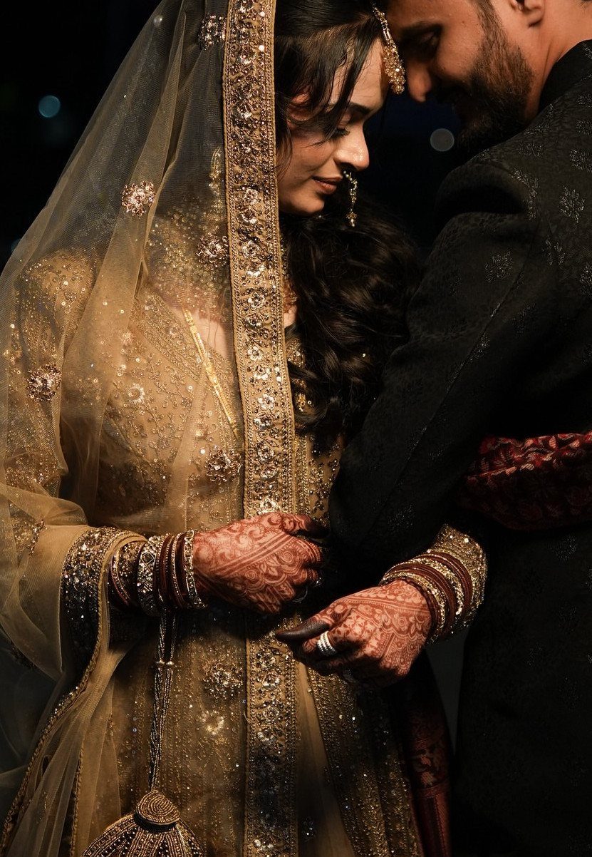 Bride in gold embroidered attire and groom in dark suit standing close together.