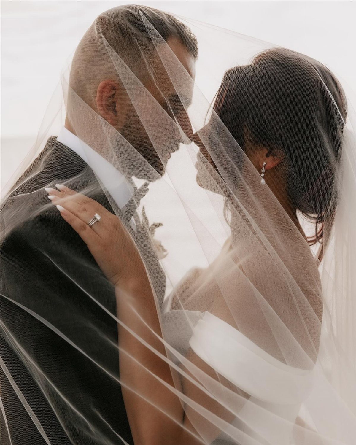 Bride and groom facing each other closely under a sheer white bridal veil.