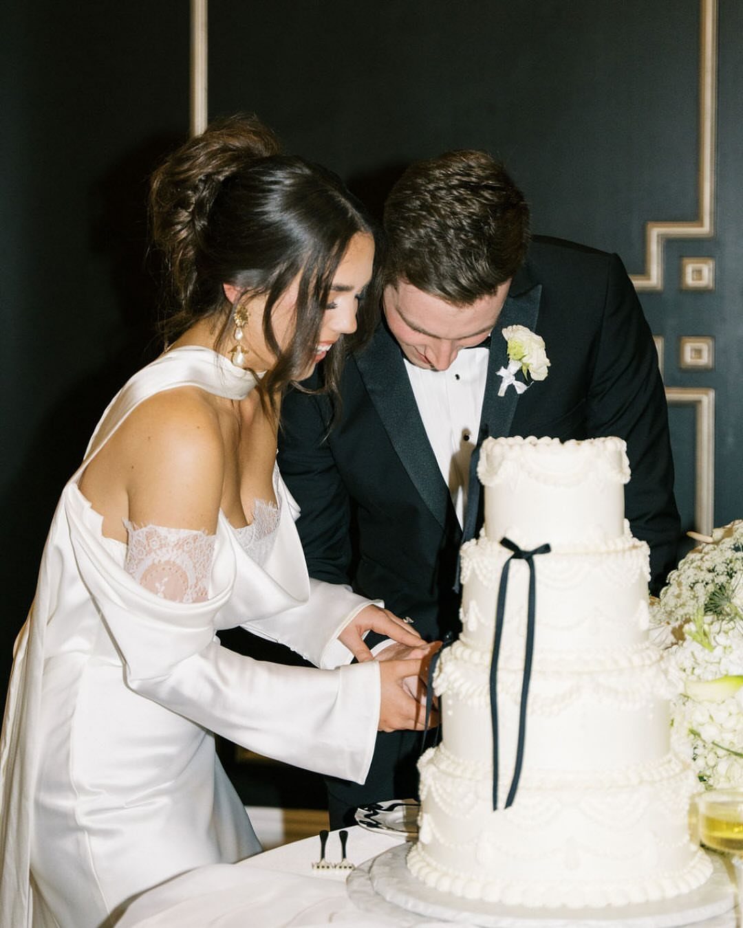 Bride and groom cutting a white multi-tiered wedding cake with black ribbons.