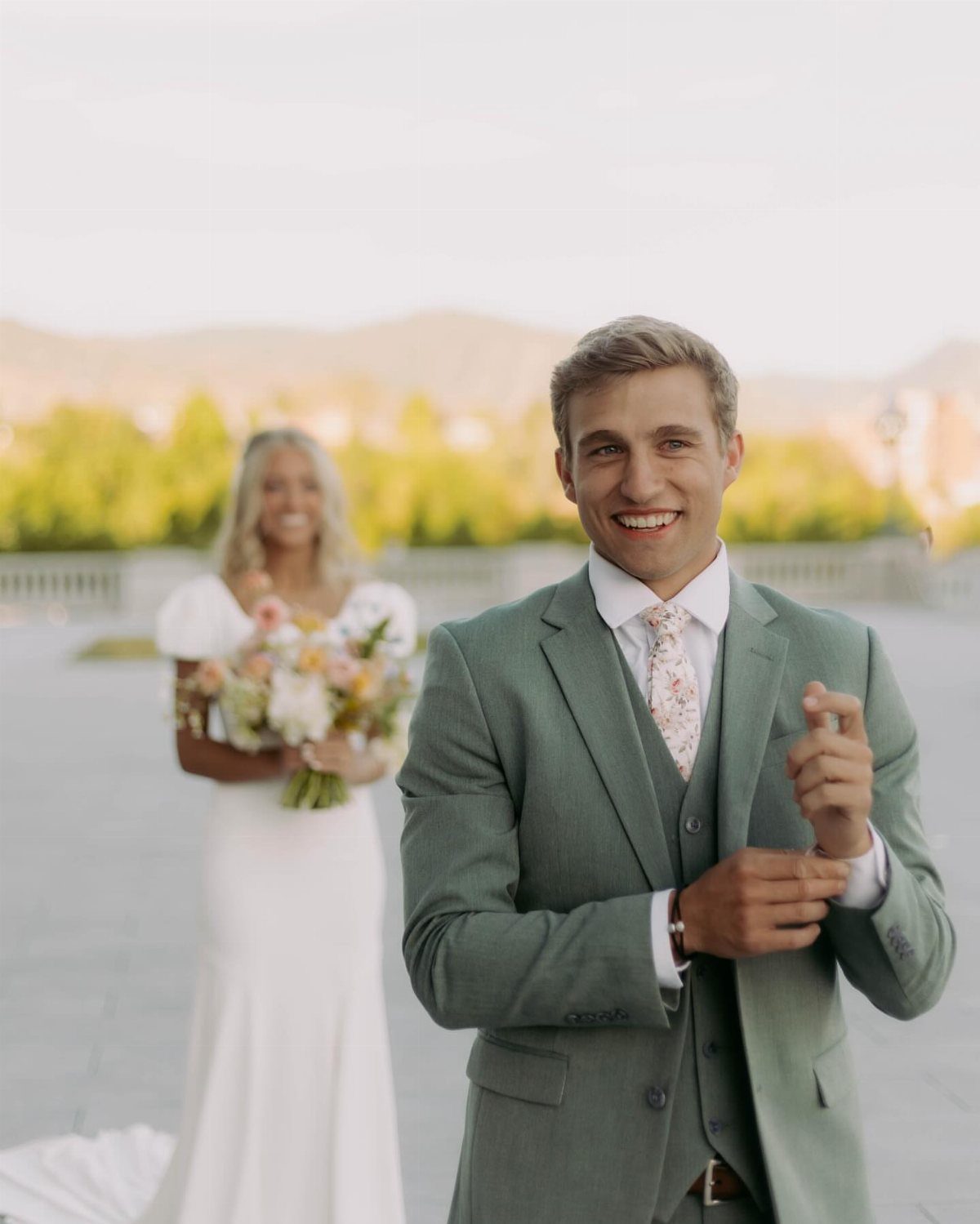 Smiling groom in green suit waiting for bride to approach him outdoors