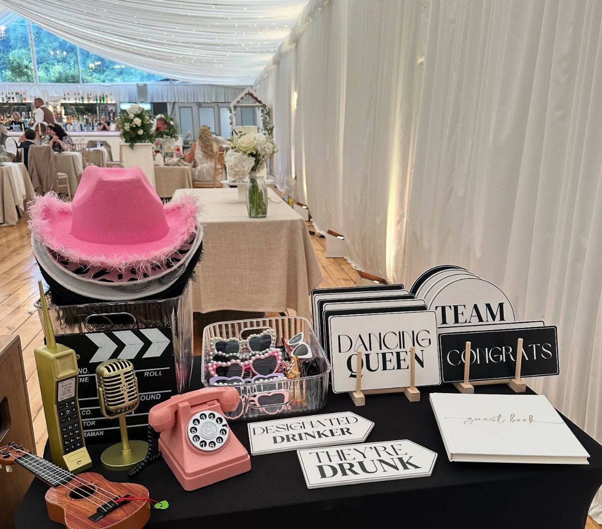 Wedding photo booth props including a pink cowboy hat, rotary phone, and signs.