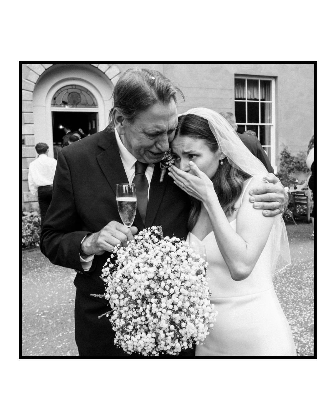 Emotional bride and father embracing during a wedding, bride holding a white bouquet.