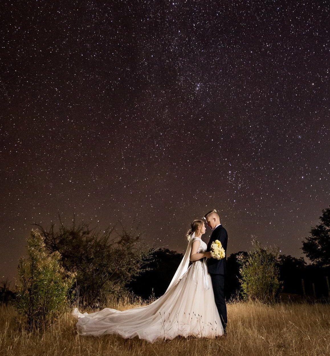 Bride and groom facing each other in a field under a starry night sky.