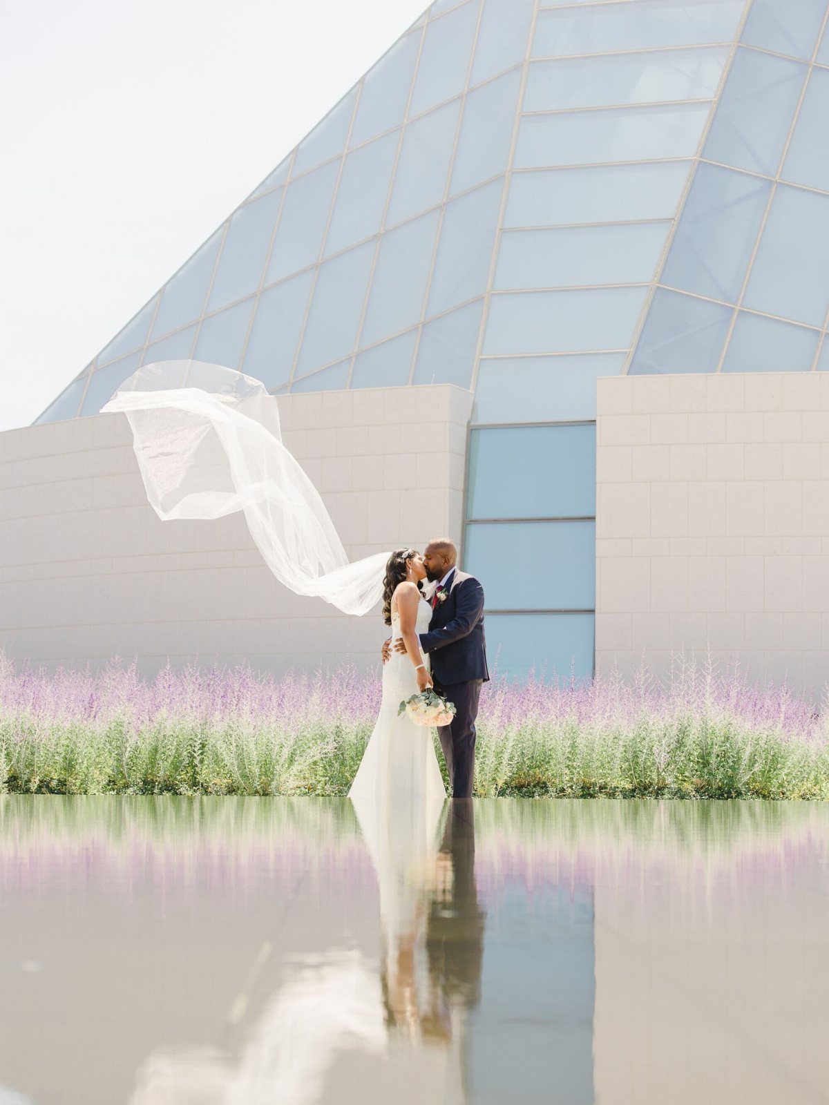 Bride and groom kissing with their reflection visible in a still water pool.