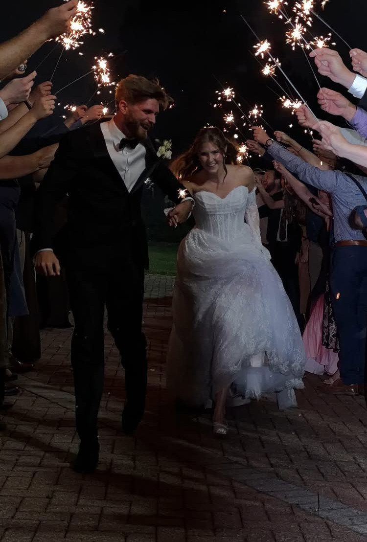 Bride and groom walking through a tunnel of guests holding lit sparklers at night.