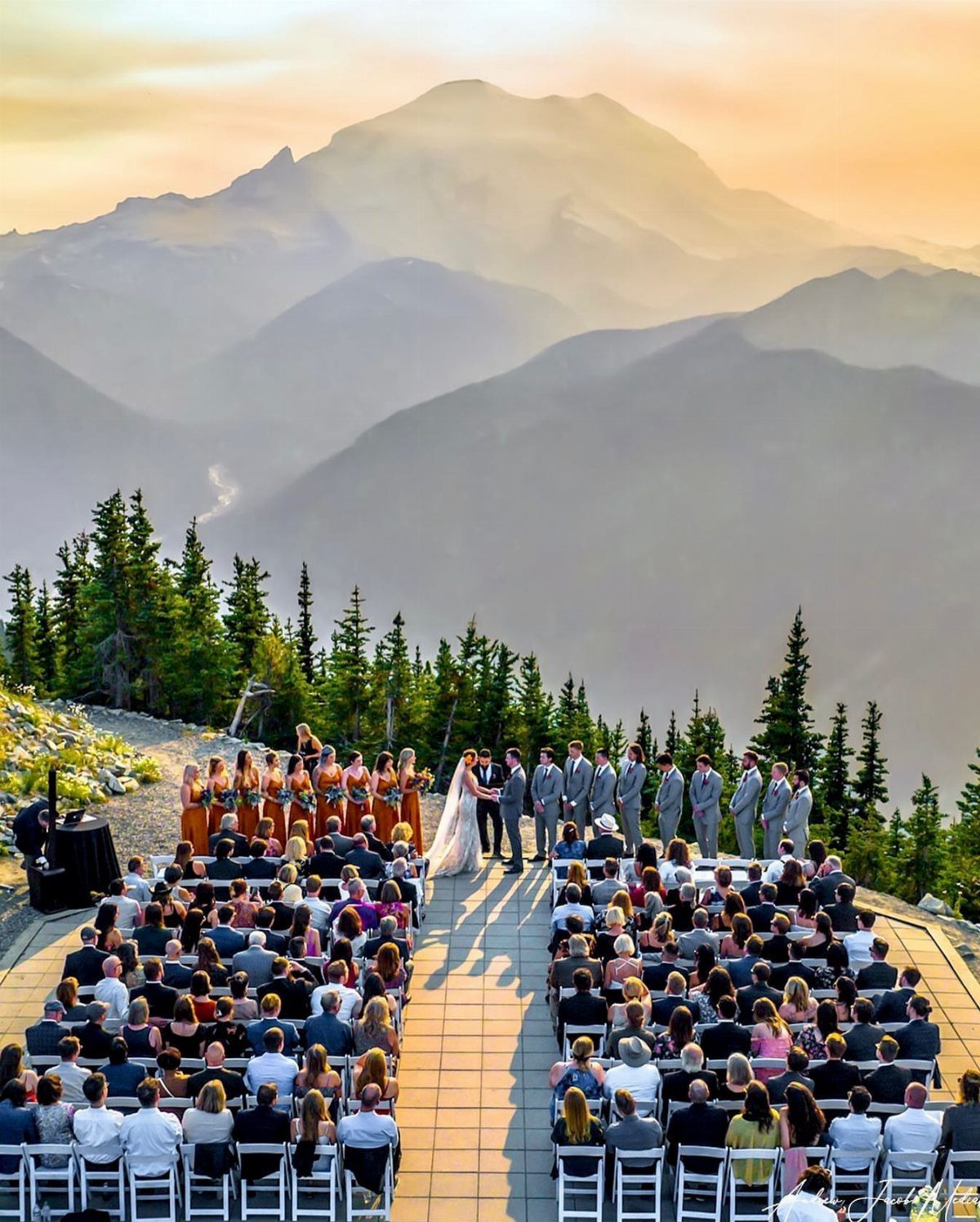 Wedding ceremony on a mountain peak with guests and a mountain backdrop.