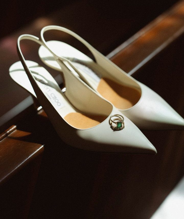 White slingback wedding shoes on a wooden surface with gold rings inside.