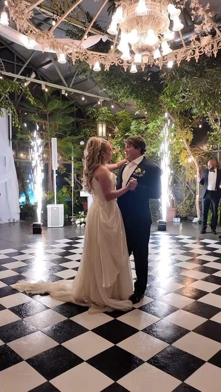 Bride and groom dancing on a checkered floor under a chandelier with sparklers.